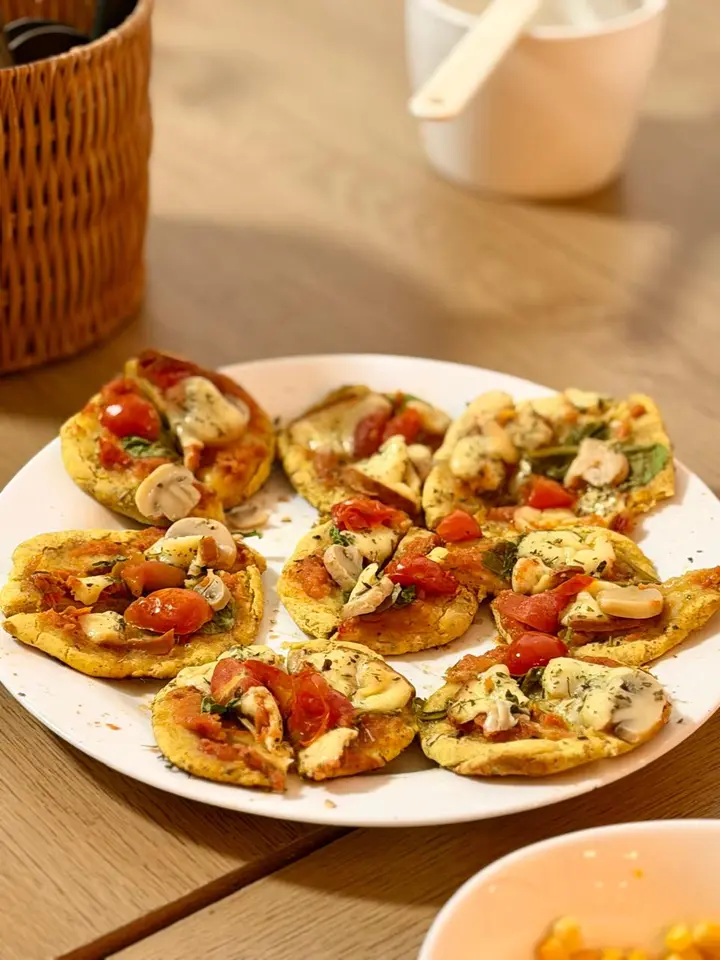 Prato com mini discos de massa cobertos de tomate, cogumelos e ervas, sobre mesa de madeira