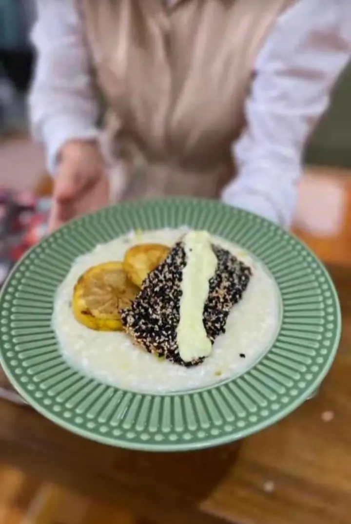 Prato verde com creme branco, rodelas de limão tostadas e uma peça coberta de gergelim